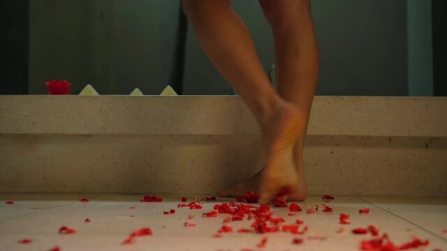 Legs of a girl walking in a bathroom with red flowers on the floor
