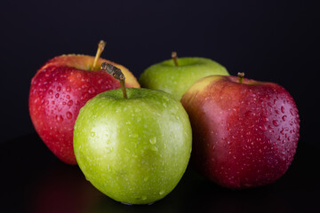 Four apples, red and green, with water droplets on a black background. Close-up vitamin.