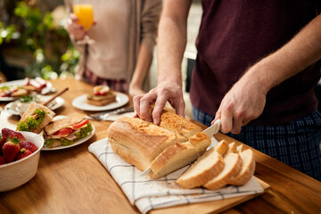 Close-up of man slicing bread at dining table.