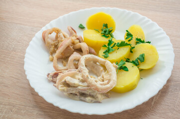 Squid rings in creamy sauce with garlic and potatoes on a white plate