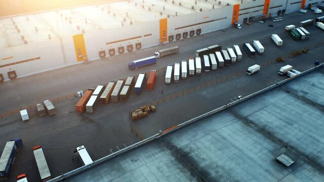 Semi-trailers trucks stand on the parking lot and wait for load and unload goods at warehouse ramps in a large logistics park with a loading hub. Aerial view