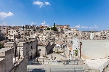 Fototapeta na wymiar Old stones buildings and ancient Italian village in Matera in Italy. Panoramic picture of white buildings made with stones. Cluster of houses. Matera, Italy. Blue sky.