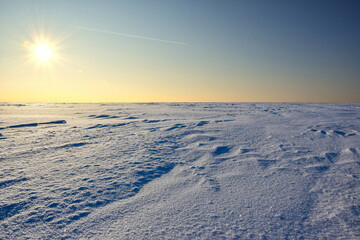 The sky is colored by the sun over a snow covered plain of fields