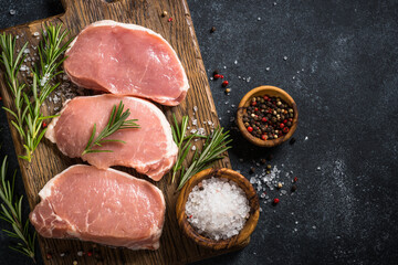 Fresh pork steaks on cutting board with ingredients for cooking.