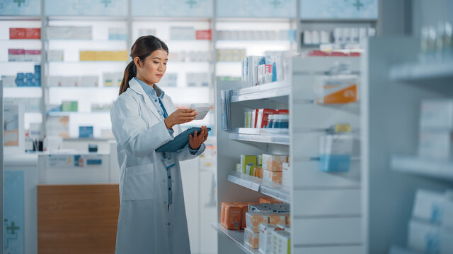 Pharmacy Drugstore: Beautiful Asian Pharmacist Uses Digital Tablet Computer, Checks Inventory of Medicine, Drugs, Vitamins, Health Care Products on a Shelf. Professional Pharmacist in Pharma Store