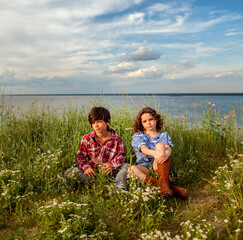 Boy and girl walking in the field with wildflowers against the background of the sea