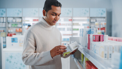 Pharmacy Drugstore: Portrait of Handsome Indian Man Choosing to Buy Medicine Browsing through the Shelf, Successfully finds what he Needs, Smiles Happily. Modern Pharma Store Health Care Products