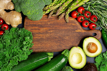 Healthy vegetarian food concept. Fresh green vegetables and herbs full of vitamins and antioxidants around wooden cutting boars. Ginger, broccoli, asparagus, cherry tomatoes, rosemary, pepper, avocado