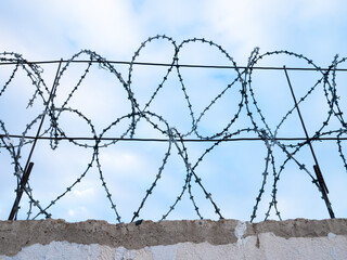 Barbed wire on the concrete fence, close-up, against the blue sky. Protected area.