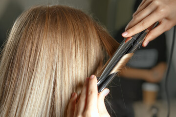Naklejka premium Hairdresser makes curls with iron to a woman client