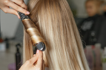 Fototapeta premium Hairdresser does curls with iron to a client