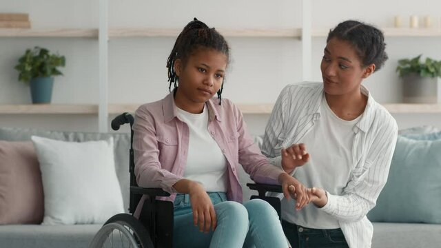Black Mother Supporting Sad Handicapped Daughter In Wheelchair At Home