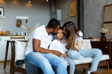 Loving black family relaxing at sofa in the morning, happy mixed race parents laughing cuddling having fun with cute little kid child son playing enjoying moments together. High quality photo