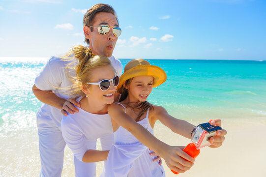 Family at the beach, mother, father and daughter taking photos, playing on the sand dressed in white tropical outfits