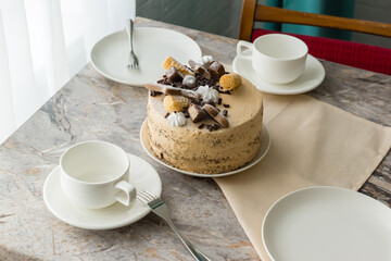 The table is set for tea: tea cups and saucers and a sponge cake with buttercream on stone countertop