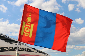 The national flag of mongolia flies against the sky.
