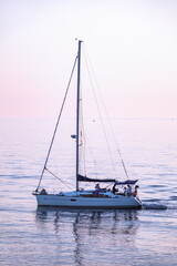 Fototapeta premium Sailing yacht in the blue sea during beautiful pink sunset.