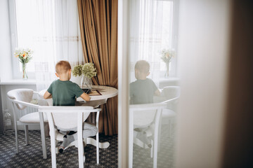 The boy plays computer games on the tablet in the kitchen.