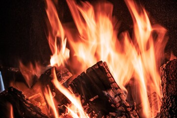 Fiery yellow orange tongues on dark background rise up in a brick fireplace burning flame, toned in red