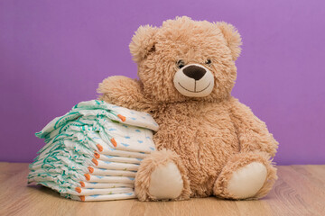 Teddy Bear relies on children's diapers. Children's toy Teddy bear and diapers on the table on the background of purple wall. Baby care concept.