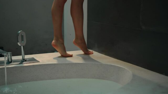 Legs of a young European girl walking around the bath on the bathroom with a crane