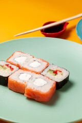 Sushi rolls in green plate on yellow background with bamboo sticks and soy sauce