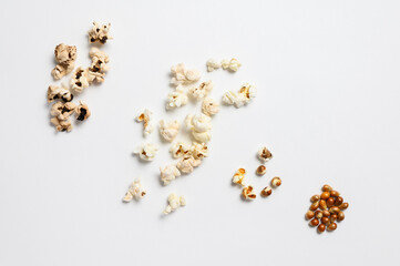 Several heaps of popcorn of varying degrees of readiness lie on a white background. Popcorns vary in readiness from raw to burnt spoiled.