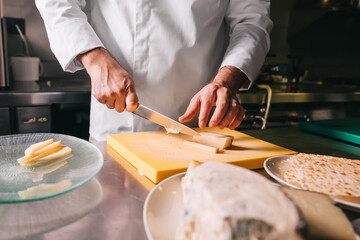 Chef's hands detail while slicing cheese on wooden cutting board