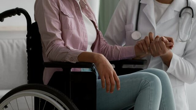 Doctor Supporting Unrecognizable Handicapped Girl In Wheelchair Indoor, Cropped