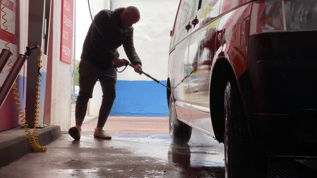 A man washing his car with pressurized water in a car wash