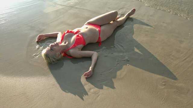Beautiful woman in bikini lying down on the sand on the sea beach. Happy woman relax on summer vacations .