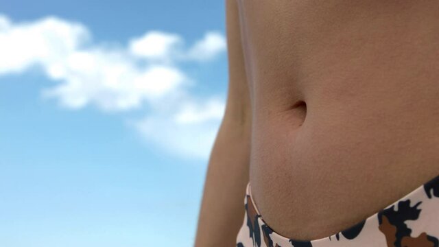 Fit and slim woman belly against blue sky. Girl on vacations in swimwear.