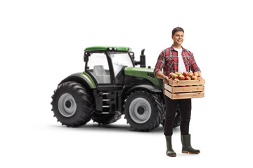 Full length portrait of a young farmer holding a crate full of fresh apples in front of a tractor