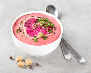 Cream soup pink watermelon radish with beetroot, parsley, sesame seeds and black flax in a bowl on a light gray background