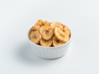 White cup with banana chips on a light background. Side view.