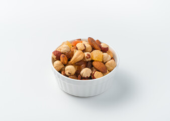 Obraz na płótnie Canvas A mixture of nuts and dried fruits in a white bowl on a light background.
