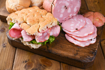 Big Italian Mortadella sausage with fat. Lunch from Focaccia with rosemary with mortadela and green salad. Traditional food from the Emilia Romagna region and the city of Bologna. Homemade food.  © Marina