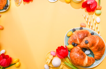 Sweet pastries on a bright background. Spring breakfast with croissants and berries. Easter chocolate eggs, red tulips on a yellow background. Copy space. Flat lay