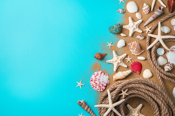 Naklejka premium Seashells of various kinds, starfish and a rope on the sand on a blue background.