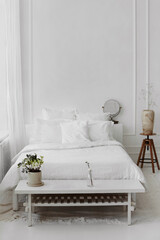Scandinavian bedroom interior of wicker armchair, bed and small wooden table with wooden vase