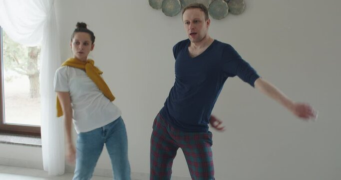 A man and a woman dance opposite a TV, parody and repeat what they show on TV. High quality 4k footage