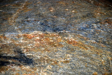 Texture of granite on a boulder stone. Close-up on the surface of a granite stone. The stone has different colors of white-brown and gray shades. The plane of the stone is not even.