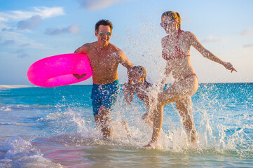 Family at the beach, mother, father and daughter in the water with pink lifesaver