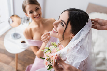 happy woman with wedding bouquet near bridesmaids fixing her veil.