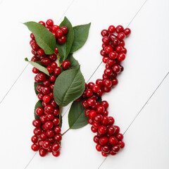 Letter k from summer harvest of cherry on white wooden background. Fruit summer alphabet. Sweet mood font. Letter K from green leaves and cherry berries. Colorful ABC, Text
