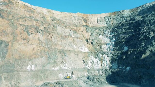 Deep open-cast mine with a drilling machine working in it. Industrial quarry, heavy industrial machinery working at the mining open pit.