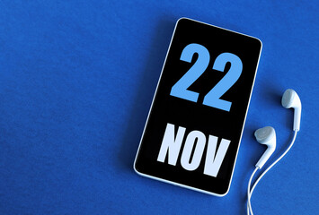 November 22. 22 st day of the month, calendar date. Smartphone and white headphones on a blue background. Place for your text. Autumn month, day of the year concept