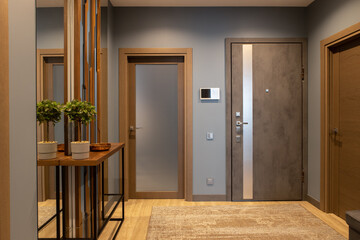 Modern entrance hallway in neutral shades of brown and gray tones in loft style. Video intercom on wall. Plant on console. Concept fashionable interior design, use of natural materials, technology