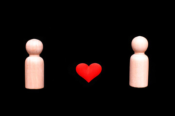 Wooden figures representing a homosexual couple of two gay men in love, with a beautiful red heart, isolated on a black background.