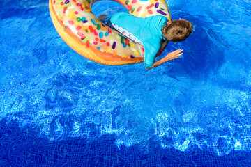 6-year-old boy bathing in a transparent pool playing with a large donut-shaped float.